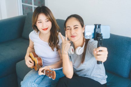 Photo for Two young adult woman living together with relationship concept. Southeast asian people couple relax lifestyle playing music on sofa life moments at home. - Royalty Free Image