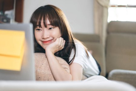 Foto de Asia student study online stay at home for new normal from virus concept. Asian teenager woman learning via internet technology with laptop. Living room background with window light. - Imagen libre de derechos