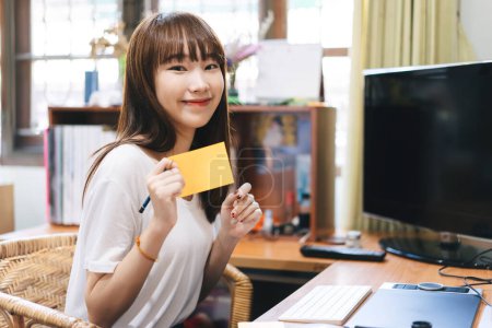 Photo for Work and study online from home office concept. Young asian cute student teenager woman hold a note paper. Background in cozy room style workplace with book. - Royalty Free Image