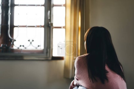 Photo for Lockdown city and people stay at home concept. Rear view of young asian teenager woman lonely and tired sit near window. Quarantine form virus corona pandemic. - Royalty Free Image
