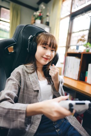 Téléchargez les photos : Portrait de femme adolescente asiatique rester à la maison avec le concept de technologie en ligne. Fille porter casque et tenant le contrôle de la joie pour jouer au jeu via Internet. - en image libre de droit