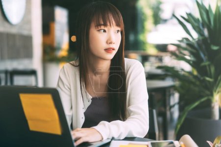 Téléchargez les photos : Jeune adulte asiatique étudiante femme utilisant ordinateur portable étude et travailler au café. Université gens ville à l'extérieur de la journée à la maison. Classe en ligne via Internet et concept d'appareil numérique. - en image libre de droit