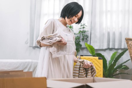 Photo for People moving house to new home or apartment concept. Happy smile woman unpack carton box in bedroom. Background cozy style room with window and copy space. Girl with short hair and casual clothing - Royalty Free Image