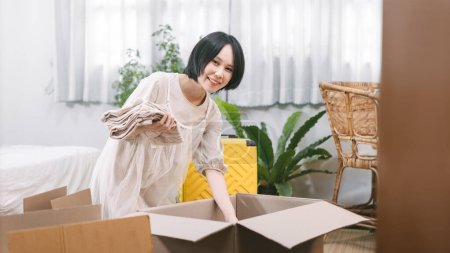 Photo for People moving house to new home or apartment concept. Happy smile woman unpack carton box in bedroom. Background cozy style room with window and copy space. Girl with short hair and casual clothing - Royalty Free Image