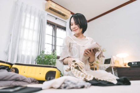 Photo for People moving house to new home or apartment concept. Happy asian woman unpack travel luggage in bedroom. Background cozy style room with window. Girl with short hair and casual clothing - Royalty Free Image