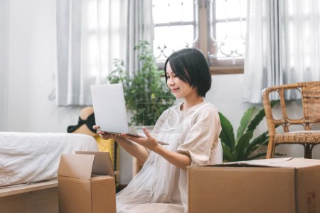 Photo for People moving house to new home or apartment concept. Asian woman unpack parcel box for new laptop in bedroom. Background cozy style room with window and carton for relocation. - Royalty Free Image
