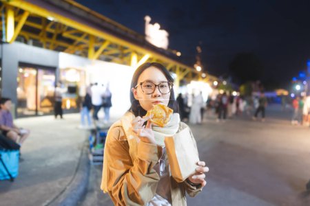 Téléchargez les photos : Poeple Voyage et manger concept de nourriture de rue. Heureux jeune adulte asiatique foodie femme tenant japonais doux à l'extérieur sur l'hiver. - en image libre de droit