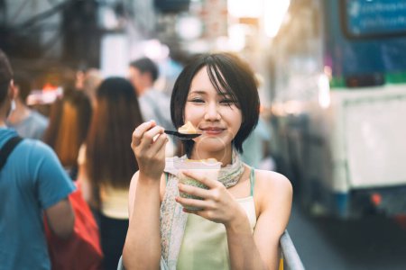 Téléchargez les photos : Heureux jeune adulte asiatique foodie womaneating thai boba dessert. Personnes voyageant avec style de vie en plein air au marché de nourriture de rue de la ville de Chine. Bangkok, Thaïlande - en image libre de droit