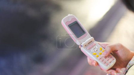 Foto de Mano adolescente usando el teléfono rosa flip para la moda de tendencia nostalgia Y2K. 2000 vibra con concepto de gadget digital. - Imagen libre de derechos
