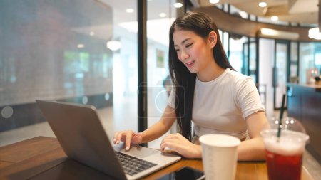 Téléchargez les photos : Entreprise indépendante jeune femme asiatique adulte utilisant un ordinateur portable pour le travail au café. Mode de vie urbain avec la technologie moderne sur le jour. Nomade numérique - en image libre de droit