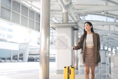 Téléchargez les photos : Freelance jeune femme asiatique adulte marchant avec des bagages de voyage pour un voyage d'affaires. Beau sourire visage cheveux longs au quai de la station le jour. Mode de vie des citadins. - en image libre de droit
