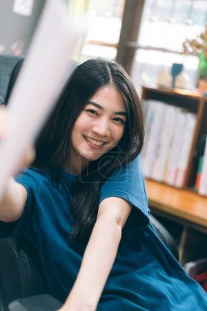Portrait von glücklichen jungen erwachsenen asiatischen Frau Gesicht lächelnd mit Zähnen. Zu Hause auf dem Sofa sitzend. Fenster mit natürlichem Licht verschwimmen.