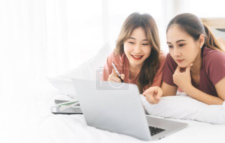 Photo for Love and togetherness of an intimate lesbian couple. Asian women living together, lying on a white bed, using a laptop for rest. Serene and joyful moments in a modern lifestyle. - Royalty Free Image