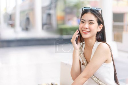 Photo for Candid portrait beautiful face asian woman with happy smile. Using smartphone and talking. Female long hair with sunglasses and shoulder bag looking up. Background with copy space. - Royalty Free Image