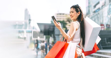 Photo for People city lifestyles with consumerism. Young adult asian woman happy smile face standing at outdoor with shopping bags. Background with copy space. - Royalty Free Image