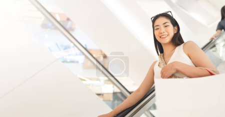 Photo for People city lifestyles with consumerism. Young adult asian woman happy smile face standing on escalator with shopping bags in department store. Background with copy space. - Royalty Free Image