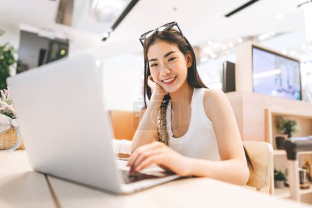 Photo for People doing freelance digital nomad job concept. Happy smile face young asian woman sitting indoors cafe on table with laptop. Influencer gen z modern lifestyles. - Royalty Free Image
