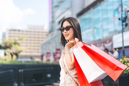 Photo for Elegant people city lifestyles with buying consumerism. Young beautiful face asian woman shopping bags wear sunglasses. Happy face standing at outdoor department store. - Royalty Free Image