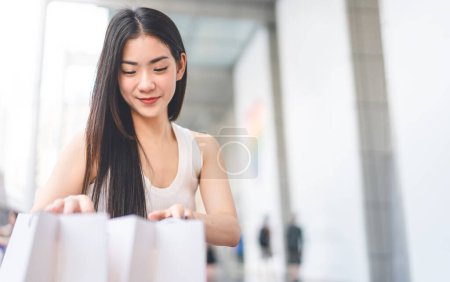 Photo for People city lifestyles travel with buying shopping consumerism. Young adult asian woman looking in shop bags. Long hair wearing white tanktop. Background with copy space. - Royalty Free Image