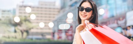 Photo for Elegant people city lifestyles with buying consumerism. Young beautiful face asian woman shopping bags wear sunglasses. Happy face standing at outdoor banner size with copy space. - Royalty Free Image