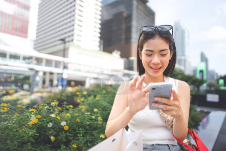 Photo for People city lifestyles with buying shopping consumerism. Young adult asian woman using smartphone typing message. Digital wallet banking payment. Happy face sitting at outdoor. - Royalty Free Image