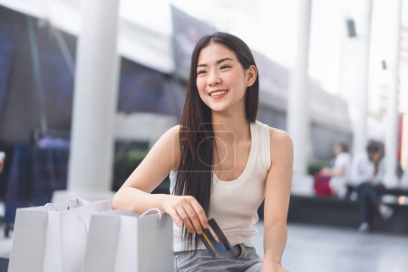 Foto de La gente de la ciudad estilos de vida con la compra de consumismo. Retrato joven hermosa cara asiática mujer sosteniendo tarjeta de crédito y bolsas de compras. Feliz sonrisa gastando dinero en vacaciones - Imagen libre de derechos