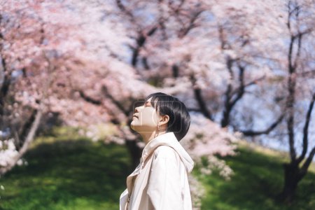 Téléchargez les photos : Vue de côté portrait belle femme japonaise avec les cheveux courts fermeture oeil. Sakura arbre de fleurs de fond. Détendez-vous dans les modes de vie floraux de la nature. Voyager au Japon vacances printemps saison. - en image libre de droit