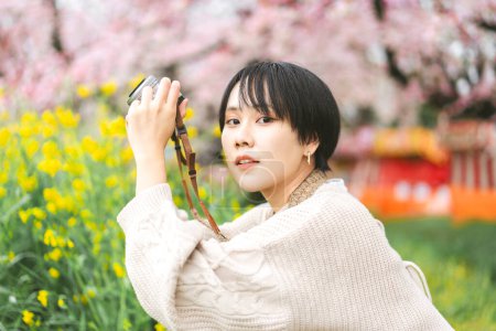 Téléchargez les photos : Vue latérale voyageur jeune femme japonaise adulte visitant sakura cerisier arbre en fleur. Mode de vie de voyage avec appareil photo. Festival Hanami au Japon au printemps Mars et Avril. - en image libre de droit