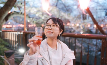 Japan Tokyo city Nakameguro sakura festival famous destination. Young adult asian woman eating strawberry sparkling wine. Japanese people lifestyles at night street sightseeing.