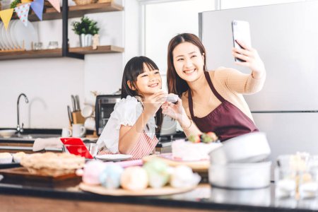 Foto de Feliz familia asiática madre e hija cocinando en la cocina. Selfie con smartphone para redes sociales. Estilos de vida de ocio en casa. Crecimiento de los niños con concepto de habilidad de interés. - Imagen libre de derechos