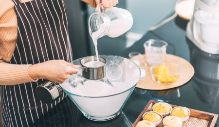 Photo for Woman hand pouring milk on measuring cup in glass bowl. Making cake at home kitchen concept. - Royalty Free Image
