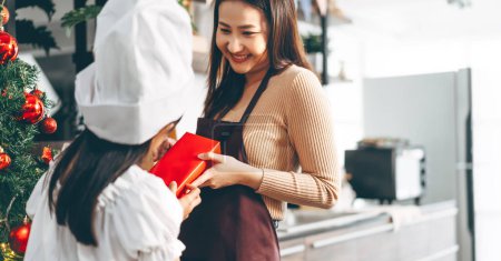 Photo for Christmas season concept. Mother giving present to her child. Celebration together with family. Happiness moment at home kitchen. - Royalty Free Image