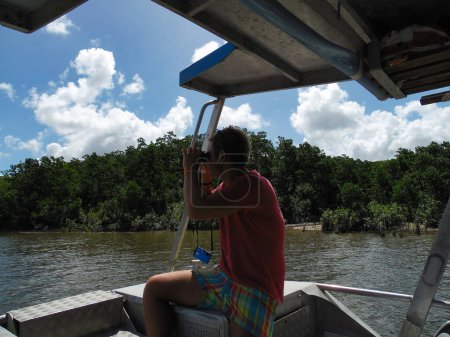 Blond man with binoculars on a boat looking for crocodiles at Kuranda river Australia Cairns. High quality photo