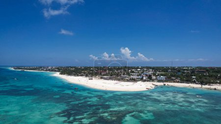 Une vue aérienne capture une petite île de Zanzibar entourée par le vaste océan. La scène comprend l'eau, les nuages, le ciel, le paysage naturel, la plage de Kendwa, les voyages, les vagues de vent et les cumulus. Afrique