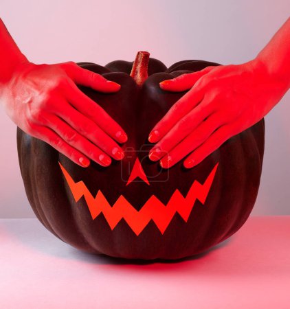 Foto de Calabaza de Halloween con papel cortado cara de miedo en la luz roja. Jack Halloween con las manos en los ojos. Sonríe Jack Calabaza. Copiar espacio - Imagen libre de derechos