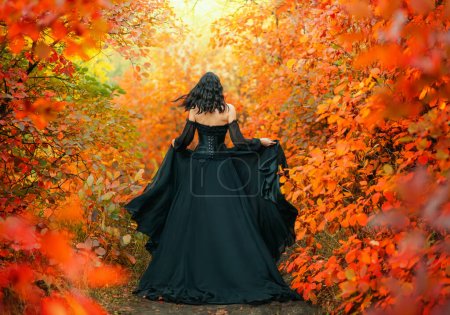 Fantasy woman runs in autumn magic forest back rear view. Long gothic black silk dress flies in wind lady witch art old style. Sexy Girl fairy princess fashion model. Orange red foliage trees. No face