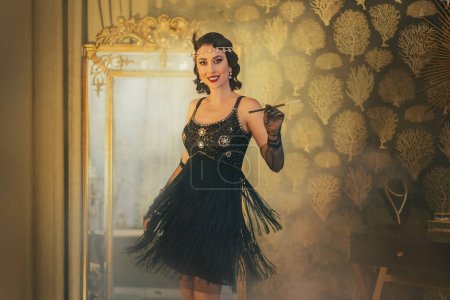 Foto de 1920s style Happy cheerful flapper woman dancing at party, short mini black fringe dress flying waving in motion. Smiling face girl holding cigarette mouthpiece. golden classic luxury interior room. - Imagen libre de derechos