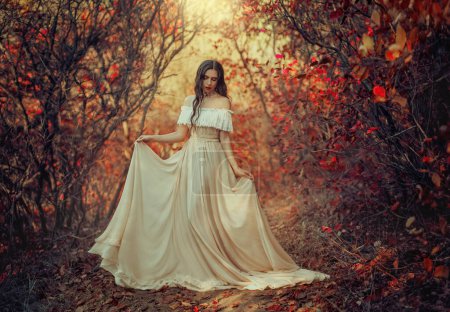 Foto de arte mujer de fantasía reina de pie en el bosque de otoño gótico, vestido de estilo vintage blanco. Chica princesa belleza cara largo cabello ondulado elegante sexy desnuda hombros abiertos. Color rojo naranja amarillo árbol oscuro