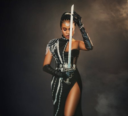 Porträt einer afrikanisch-amerikanischen Kriegerin, die eine Schwertwaffe in der Hand hält. Dunkle Königin Mädchen im schwarzen Militärkostüm. Gotische Elfenfee. Sexy Schönheit Gesicht Mode-Modell beten. Studiofoto.