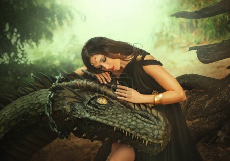 Photo for Fantasy woman evil dark queen witch hugs dragon, touching with hands head. Girl mistress tamed myth monster, concept of dominance control. black dress girl princess fashion model, golden moon diadem. - Royalty Free Image