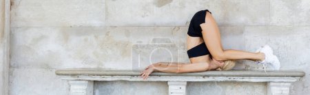 Femme de sport blonde en crop top noir, shorts et baskets blanches s'entraînant sur banc en pierre à l'extérieur en Italie, bannière 