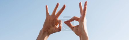Photo for Cropped view of woman showing ok gesture with blue sky at background, banner - Royalty Free Image