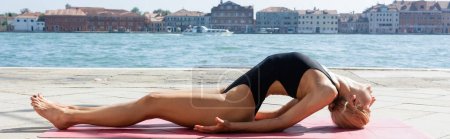 Téléchargez les photos : Vue latérale de la femme blonde pratiquant le yoga asana sur tapis à Venise, bannière - en image libre de droit