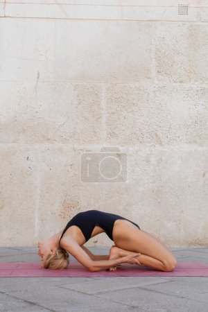 Photo for Side view of blonde woman practicing yoga kapotasana pose on sidewalk in Venice - Royalty Free Image