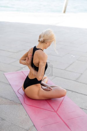 Blonde Frau praktiziert Yoga auf rosa Yogamatte auf Bürgersteig in Venedig 