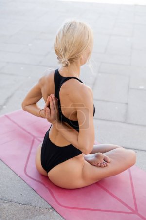 Rückansicht einer meditierenden Frau in Feuerklotz-Pose, während sie im Freien auf einer Yogamatte sitzt 