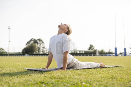 nivel superficial del hombre joven del yoga que practica la pose de la cobra con los ojos cerrados en la hierba verde al aire libre