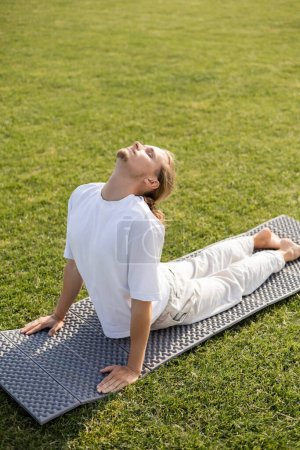 young bearded man with closed eyes meditating in cobra pose on yoga mat 
