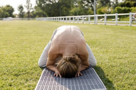 Photo for Shirtless man with long hair meditating in himalayan duck pose on yoga mat on grassy field - Royalty Free Image