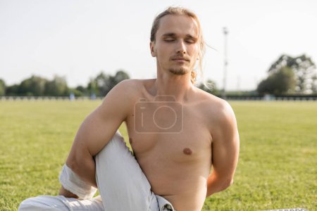 calm and shirtless man with closed eyes practicing yoga in sage pose outdoors